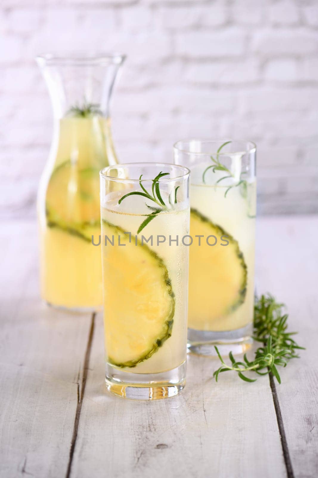 A glass of lemonade with pineapple pieces, ice cubes and rosemary. Cold refreshment organic non-alcohol cocktail.