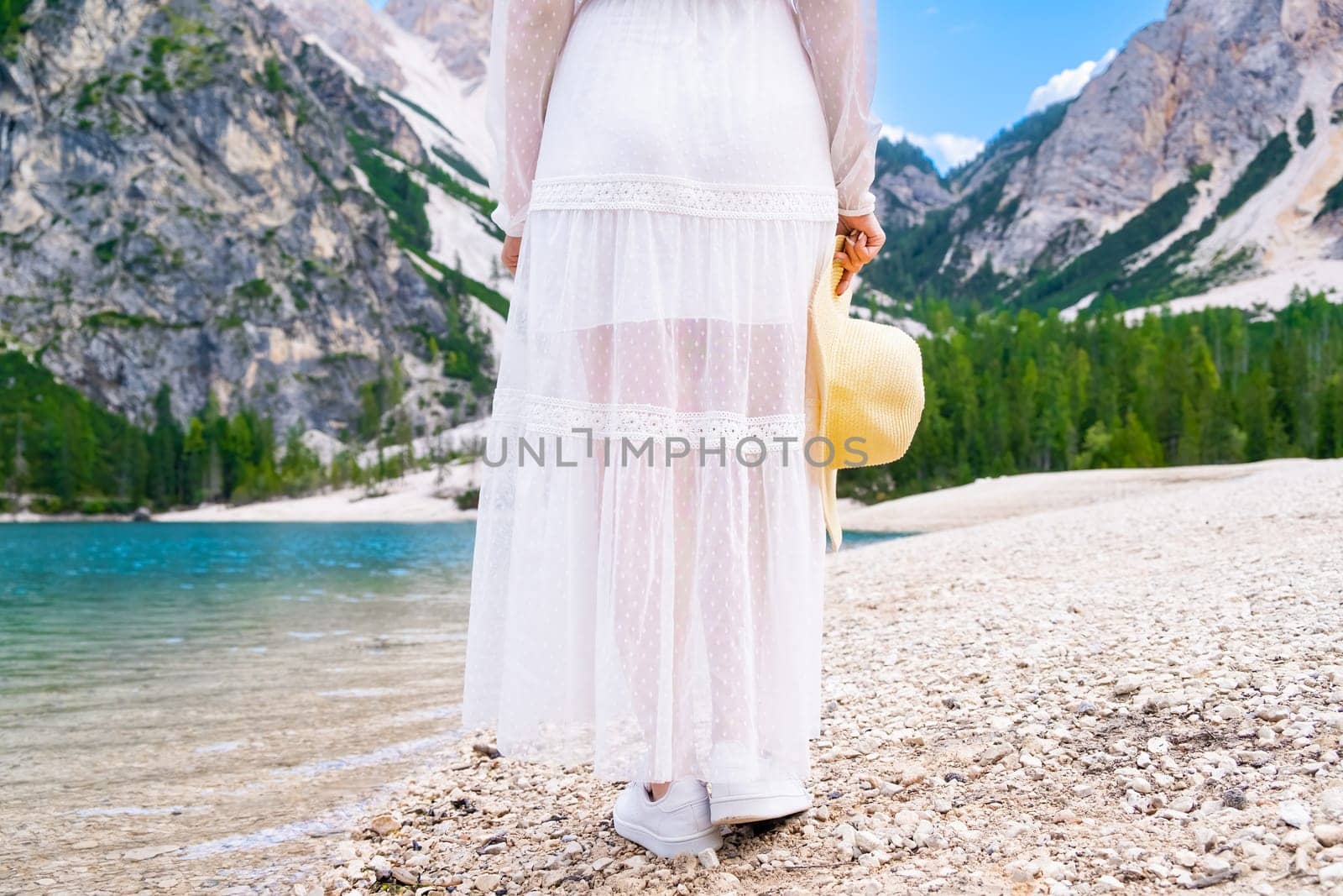 A young woman walks along the Lake Braies in a white dress and hat in her hands by vladimka