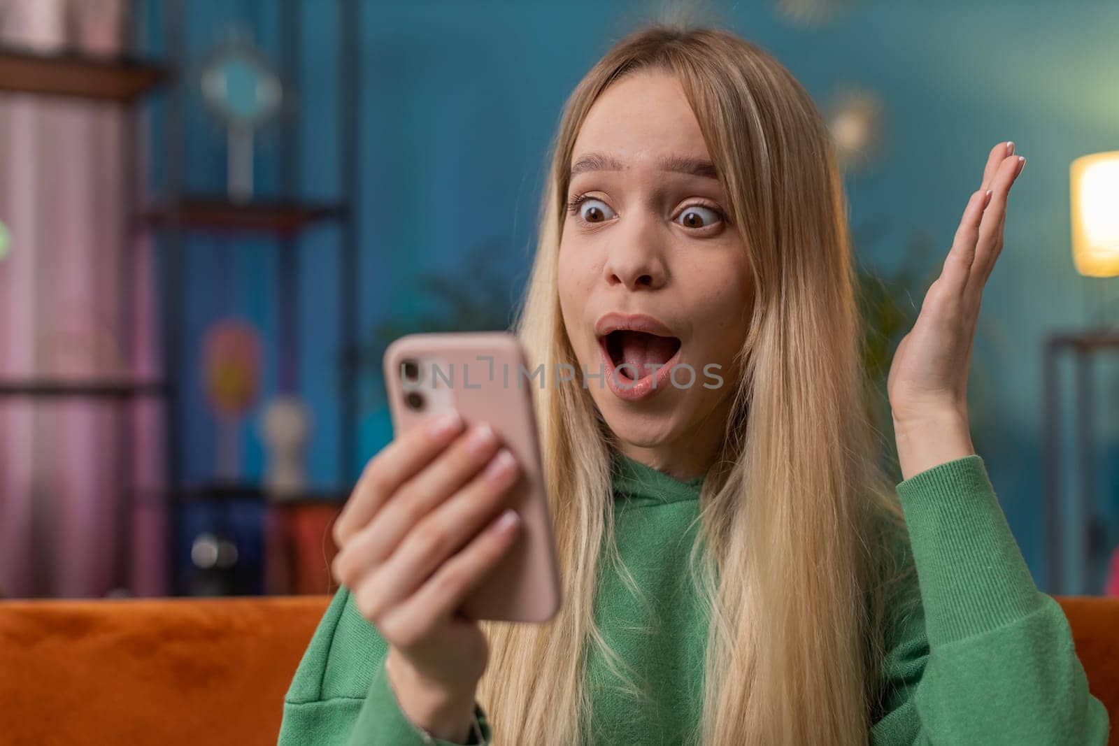 Oh my God Wow. Excited happy young woman use smartphone typing browsing celebrating success winning, lottery jackpot goal achievemen, good news, victory. Caucasian girl holds mobile phone at home room
