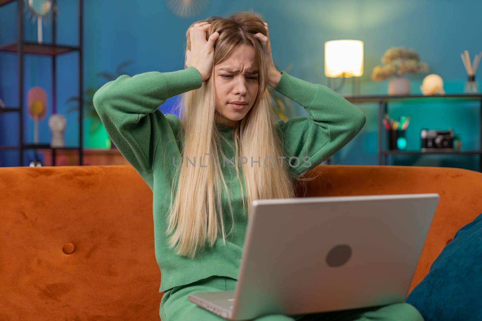 Displeased Caucasian woman use laptop notebook typing browsing working, loses becoming surprised sudden lottery results bad news fortune loss fail computer virus. Young girl at home in room on couch