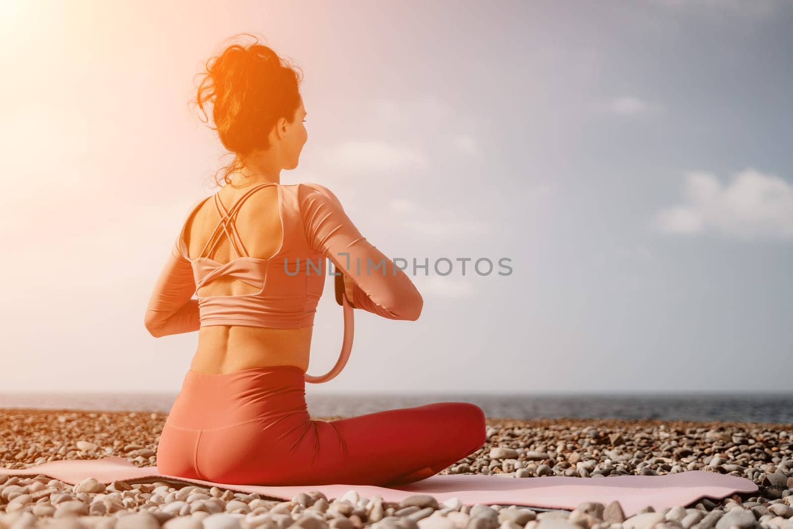 Woman sea pilates. Sporty happy middle aged woman practicing fitness on beach near sea, smiling active female training with ring on yoga mat outside, enjoying healthy lifestyle, harmony and meditation by panophotograph