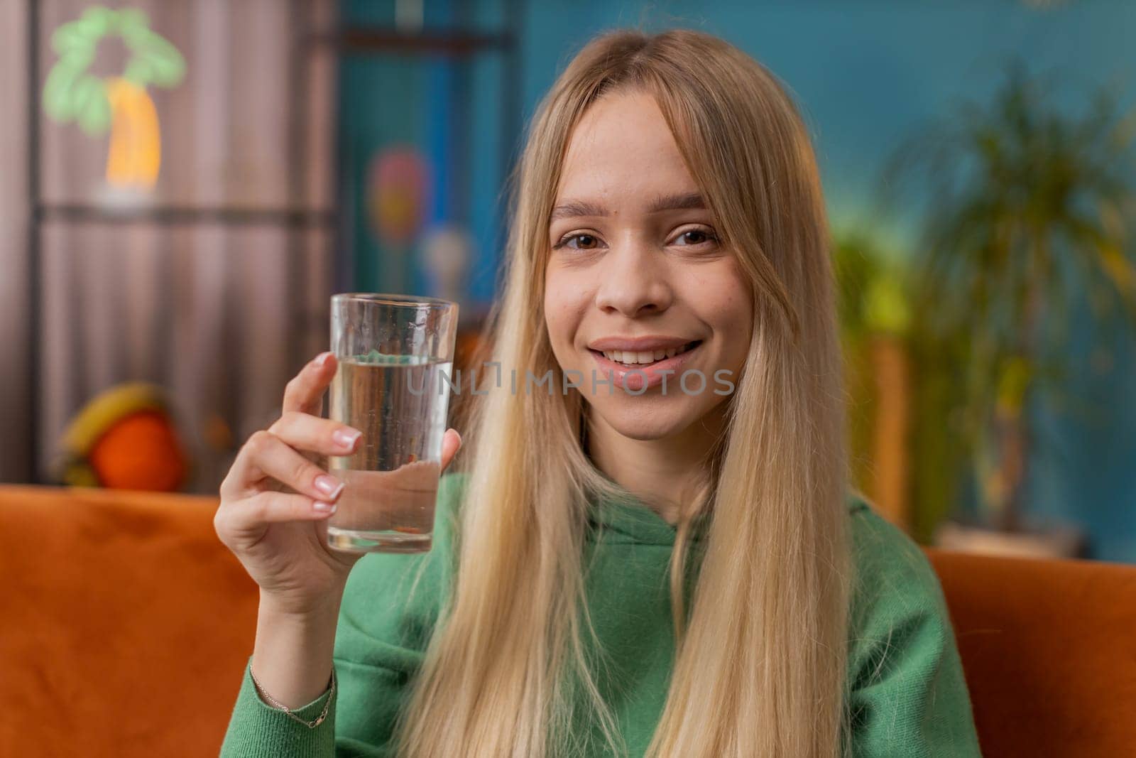 Thirsty woman holding glass of natural aqua make sips drinking still water preventing dehydration sits at home living room. Caucasian girl with good life habits, healthy slimming, weight loss concept