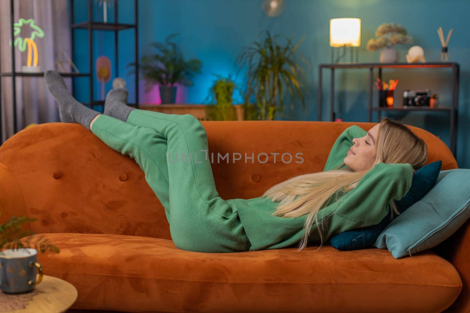 Tired young woman lying down on comfortable couch, taking a rest, daytime nap. Portrait of carefree teen girl holding hands behind head relaxing, falling asleep at home apartment living room on sofa