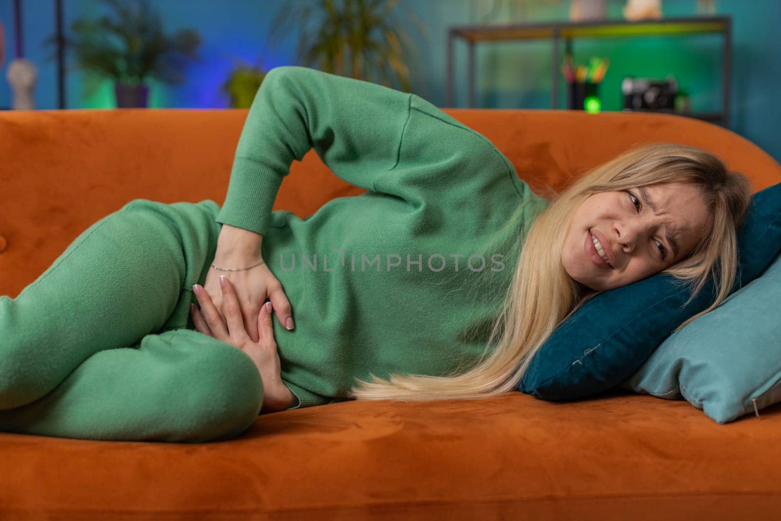 Sick ill woman suffering from period cramps, painful stomach ache lying on sofa at home room. Girl holding belly, feeling abdominal or menstrual pain. Abdominal pain, gastritis, diarrhea, indigestion