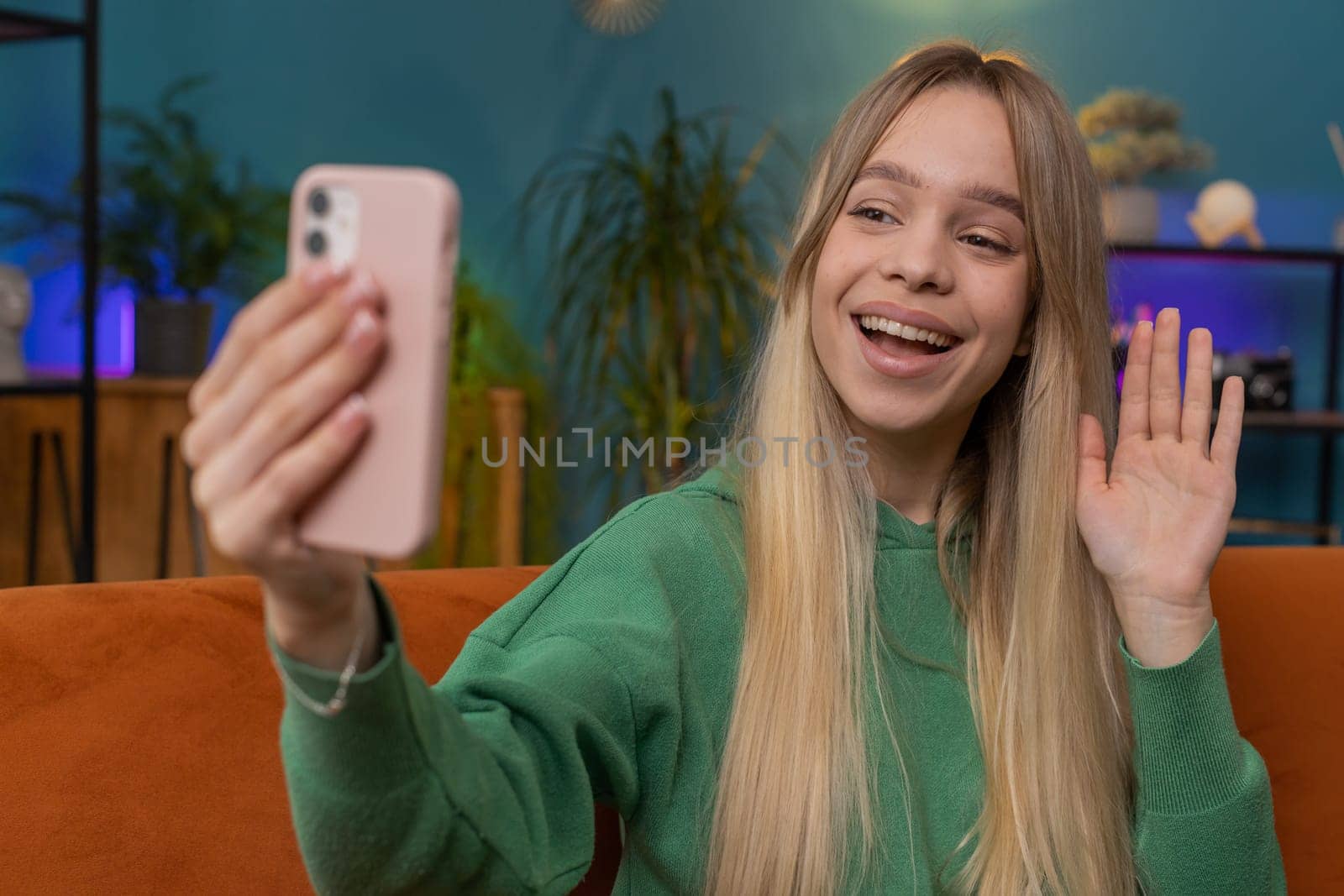 Happy woman blogger taking selfie on smartphone, communicating video call online with subscribers, recording stories for social media. Portrait of Caucasian girl at home apartment living room on sofa