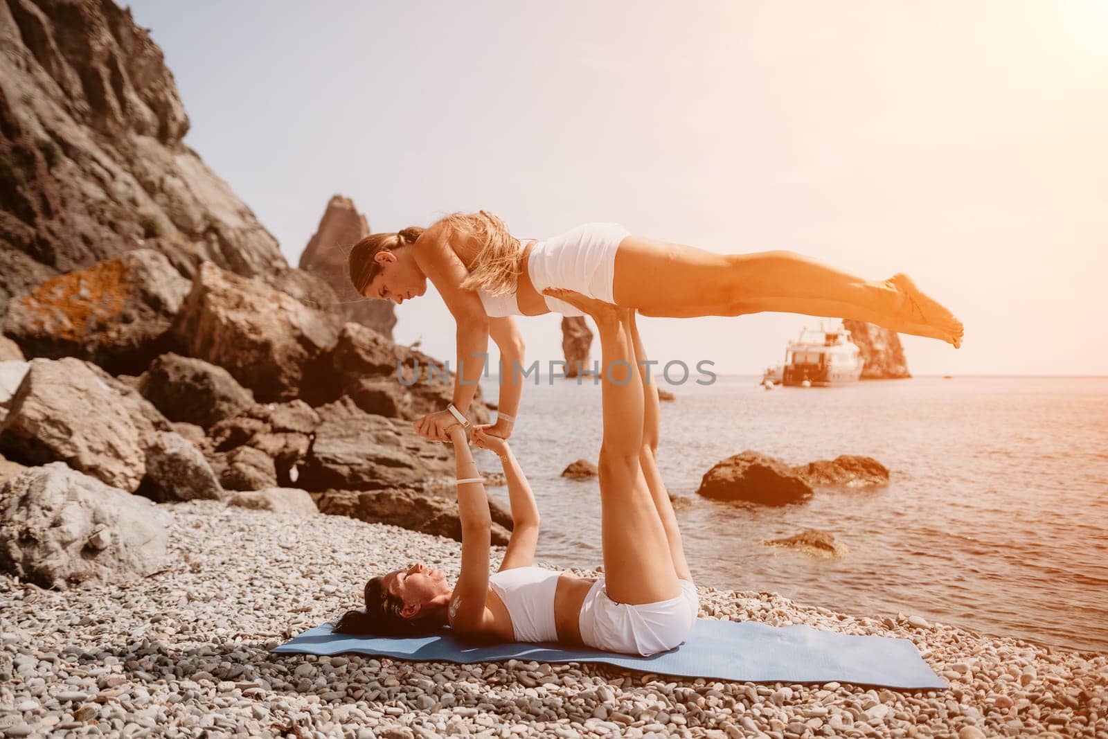 Woman sea yoga. Two Happy women meditating in yoga pose on the beach, ocean and rock mountains. Motivation and inspirational fit and exercising. Healthy lifestyle outdoors in nature, fitness concept. by panophotograph