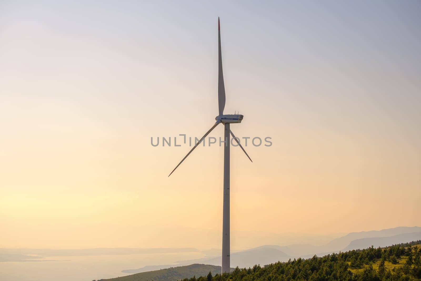 Wind turbine produces electrical green energy standing on coast of Adriatic Sea. Huge windmill converts wind power into electricity at sunset