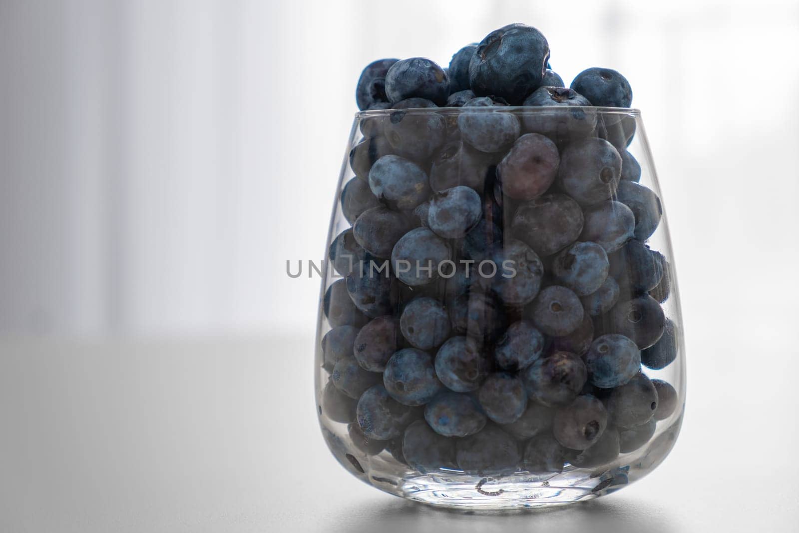 Blueberry in the glass standing on the white table by vladimka
