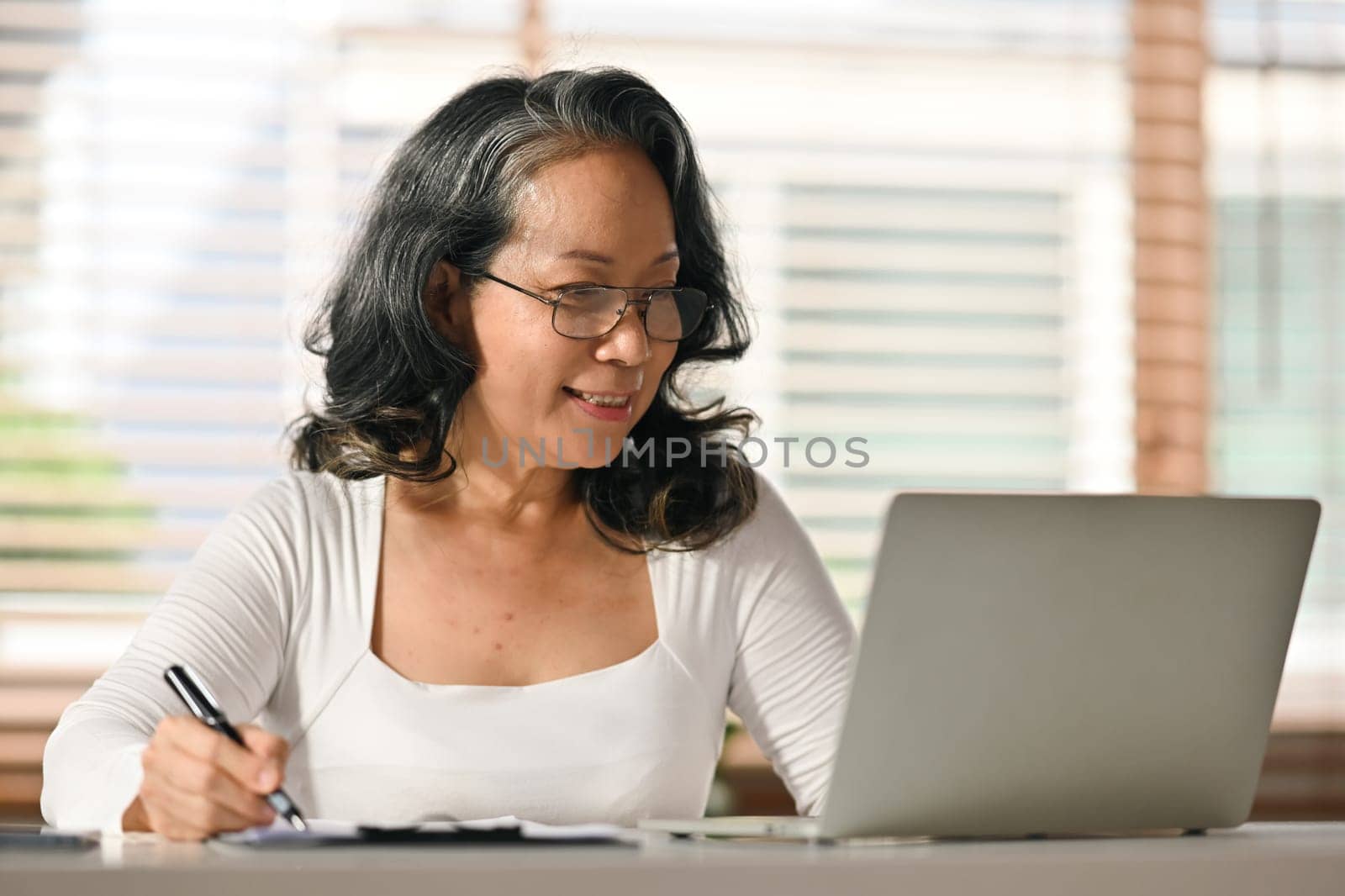 Senior woman reading online news, browsing internet on laptop at home. Retired lifestyle and technology concept.