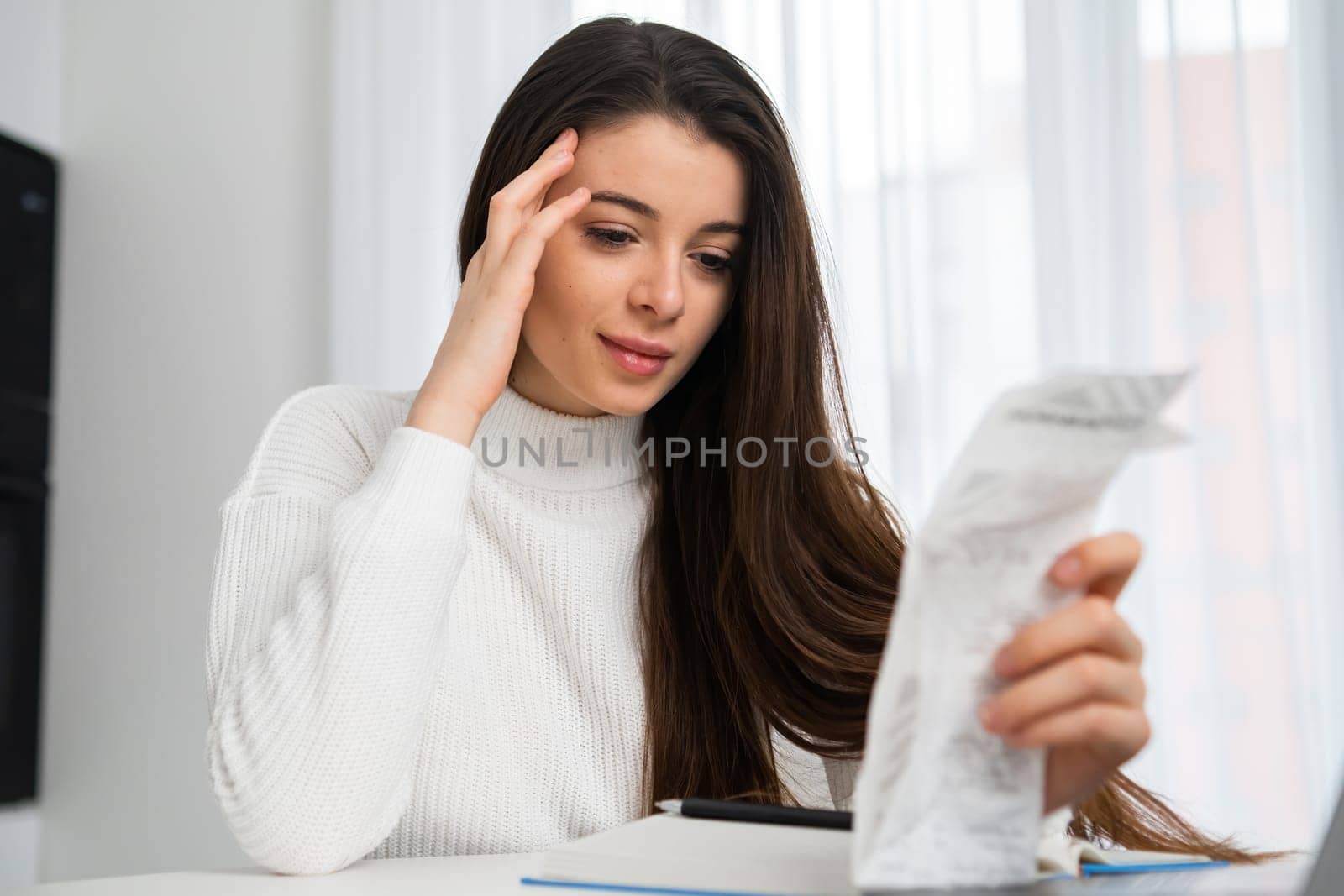 Beautiful woman holding paper bill planning finance and calculating money budget at home