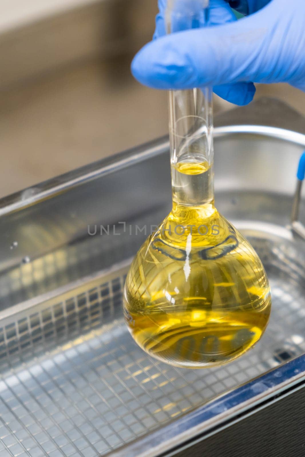 Scientist in blue rubber puts a yellow solution in the flask for dissolving or extraction into ultrasound bath. Urea analysis. Clinical, toxicological and forensic analysis.