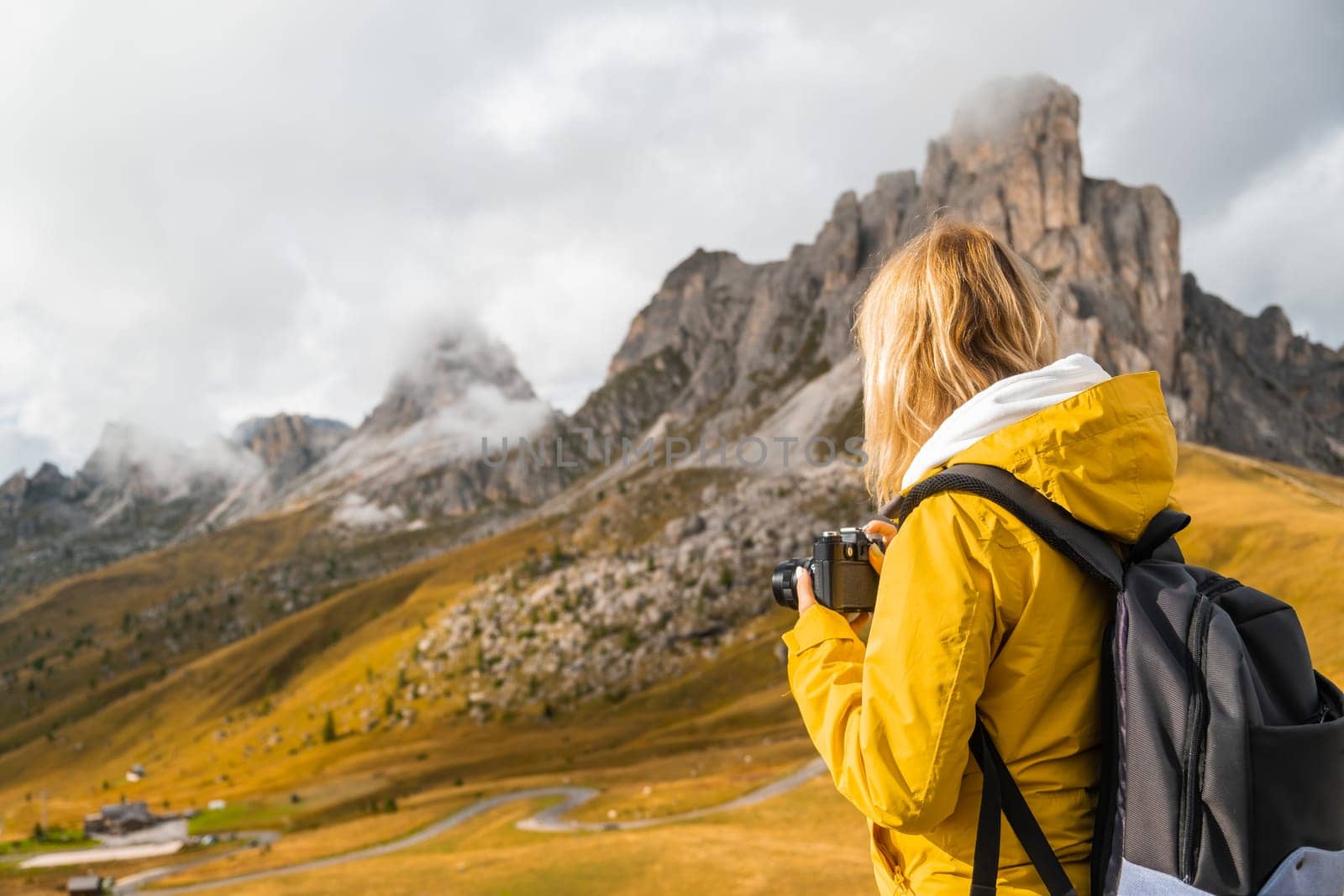 Blonde tourist captures moments on camera and enjoys vacation on Alpine mountains. Woman makes photos of mountain hills covered with clouds