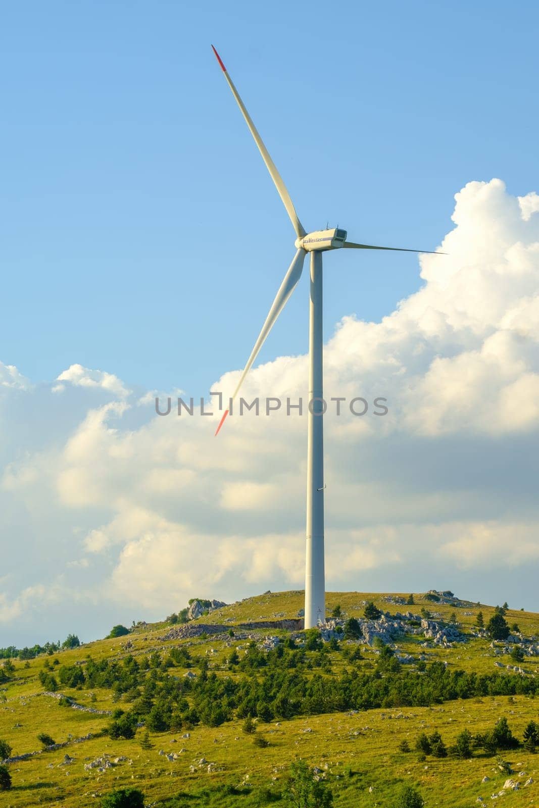 Wind turbine produce electrical green energy from kinetic energy. Tower stands on hill generating renewable power against blue sky with clouds