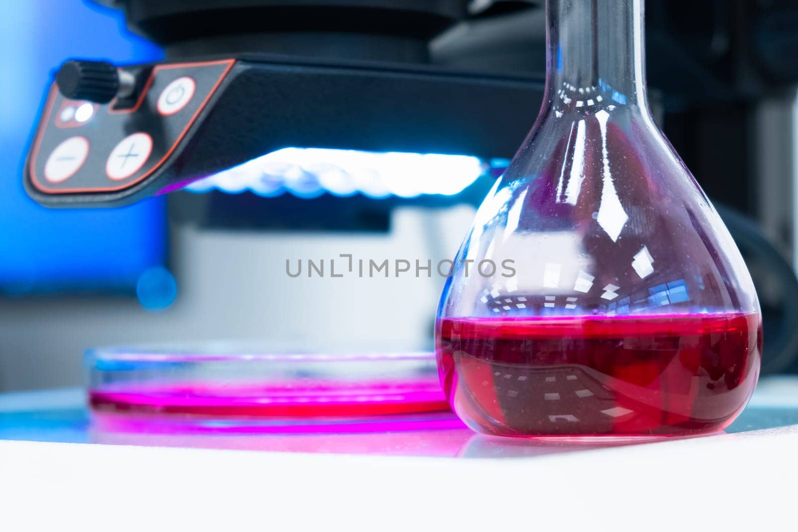 Round flask with colored liquid or blood sampleon the table in a modern laboratory with a microscope on the background.