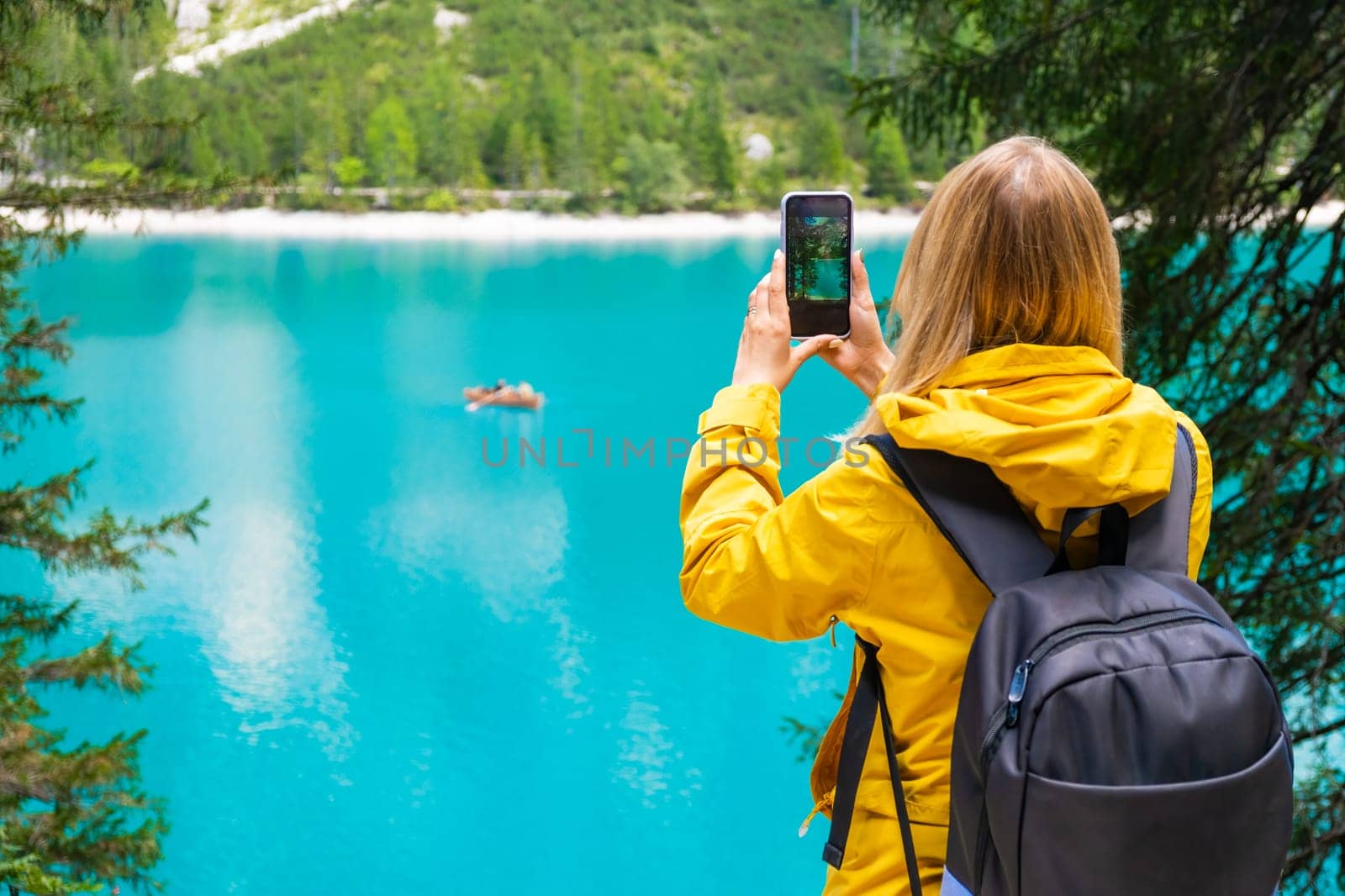 Tourist takes photo of the stunning lake Braies in the Dolomite mountains with turquoise water and wooden boats.