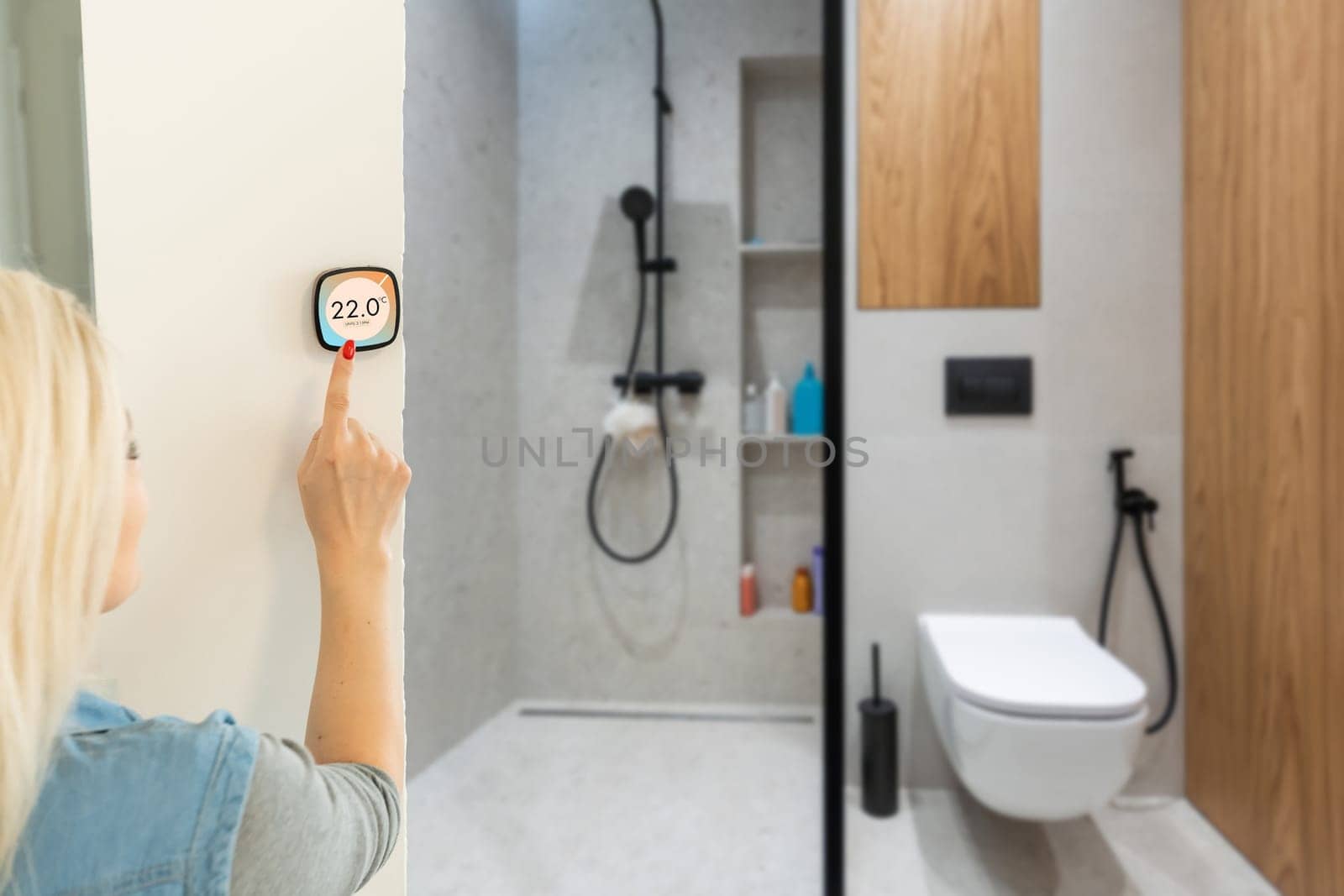 Smiling Indian woman using modern smart home system, controller on wall, positive attractive young female switching temperature on thermostat or activating security alarm in apartment. by Andelov13