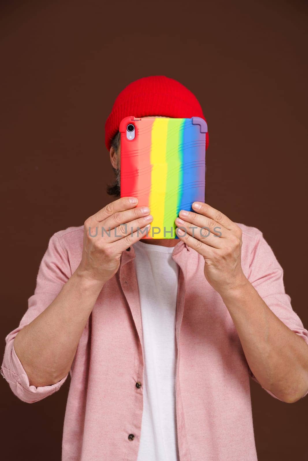 Incognito internet gay user. The man hides his sexual orientation online, covers his face with tablet in rainbow case, as symbol LGBTQ. High quality photo