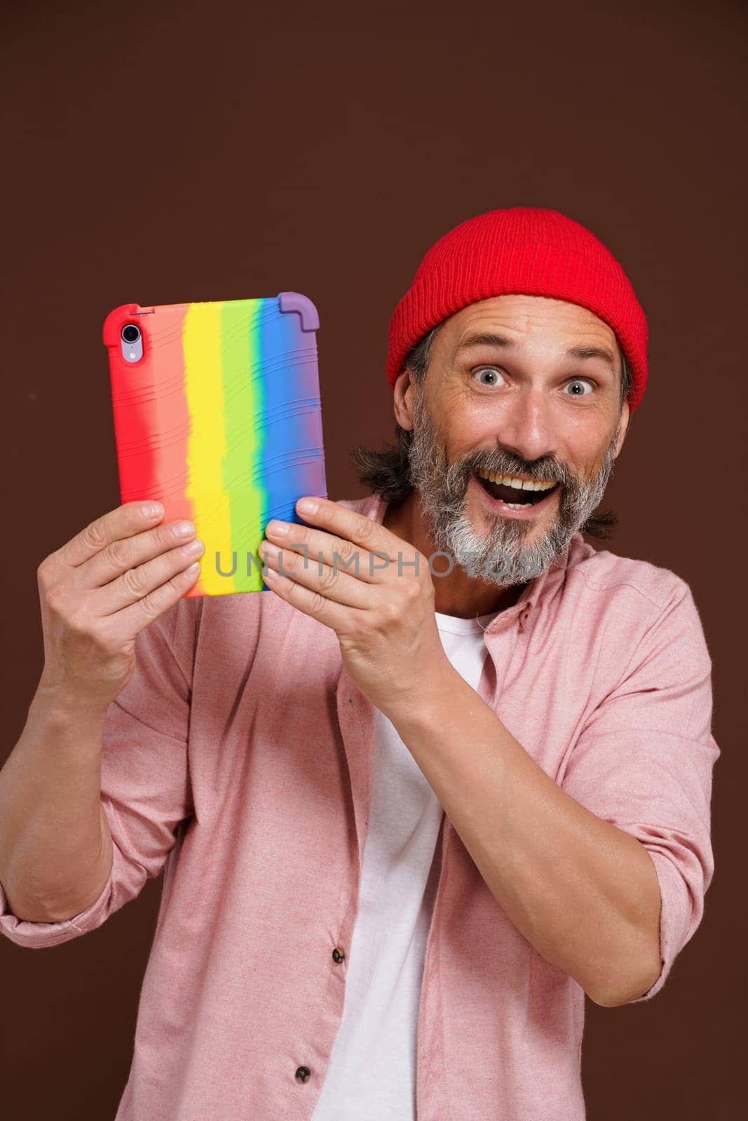 Coming out LGBTQ concept. Happy European man smiling while holding tablet PC in colorful rainbow case. Modern man with digital device represents LGBTQ community. by LipikStockMedia