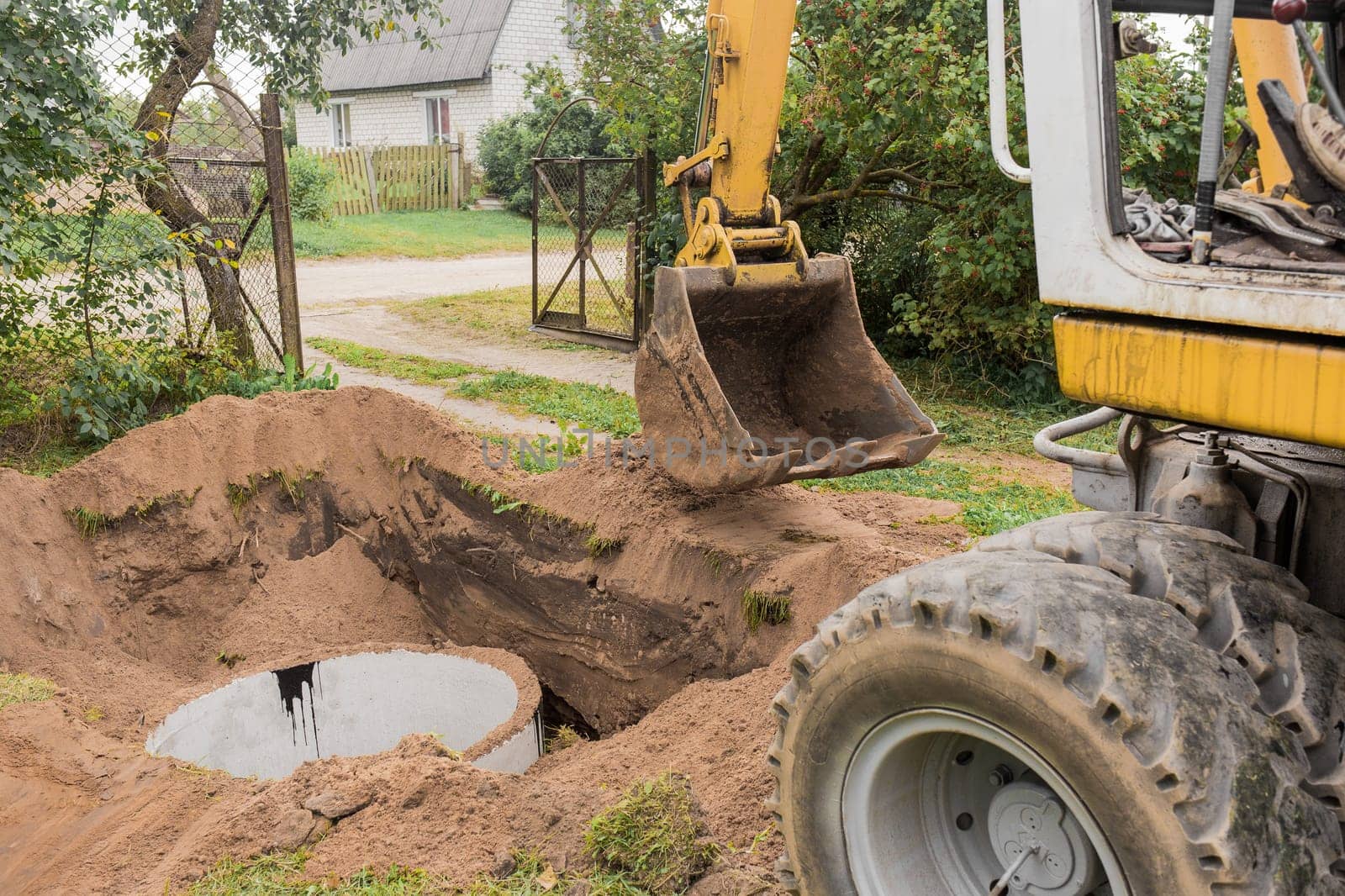 A bucket of excavator with a pile of sand and earth buries sewer concrete rings in the industrial zone by AYDO8