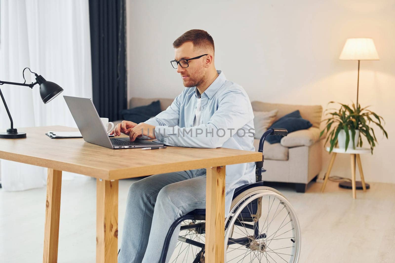 Working by using laptop. Disabled man in wheelchair is at home.
