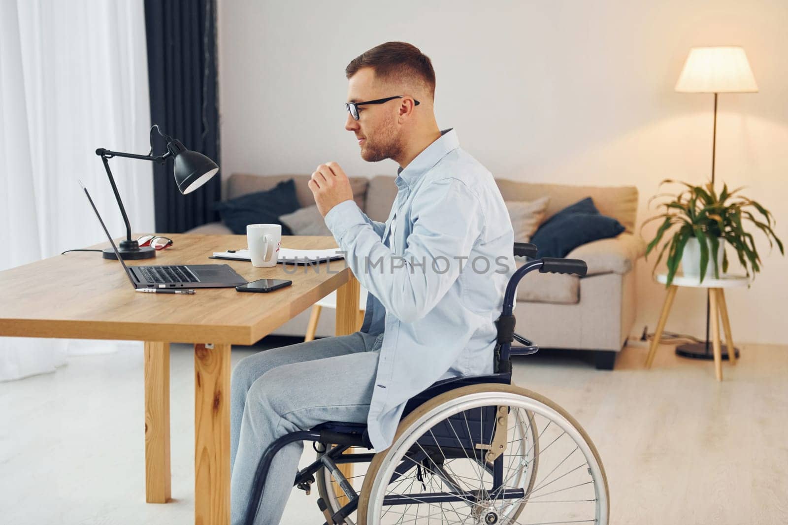 Working by using laptop. Disabled man in wheelchair is at home.
