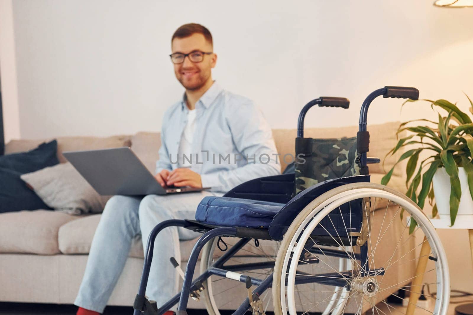 With laptop on the legs. Disabled man in wheelchair is at home.