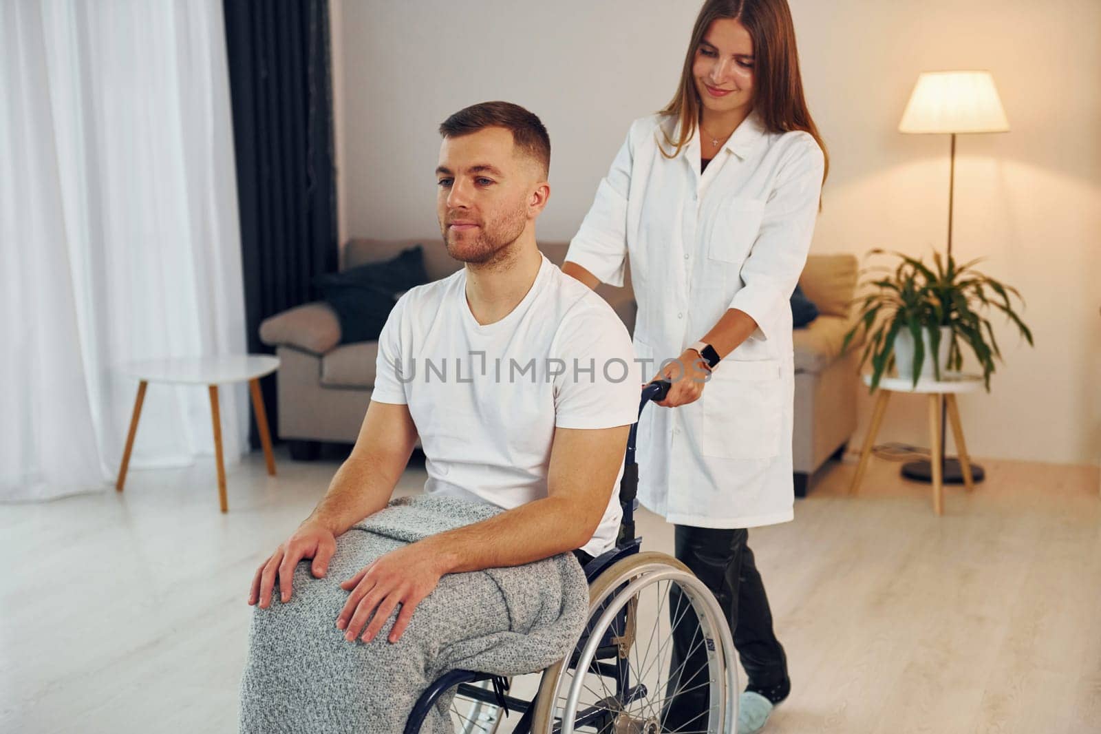 Medical worker. Woman is helping. Disabled man in wheelchair is at home.