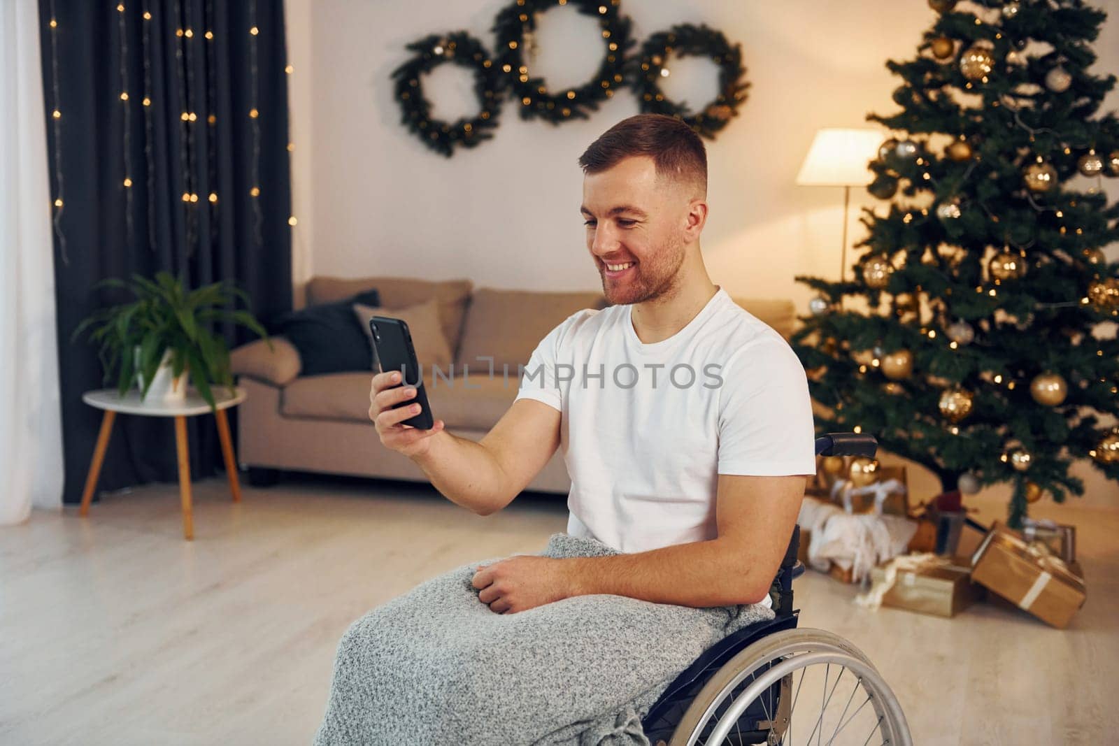 Using smartphone to communicate with people. New year is coming. Disabled man in wheelchair is at home.