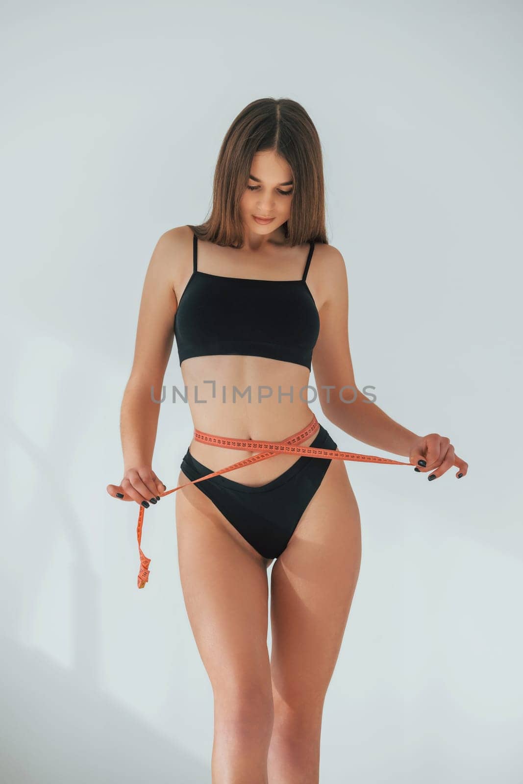 WIth measuring tape. Beautiful woman in underwear is posing indoors.