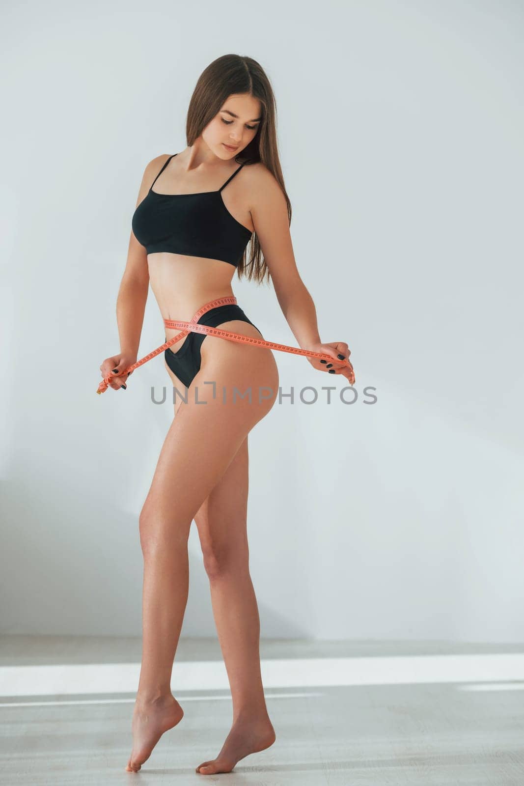 Measuring the waist. Beautiful woman in underwear is posing indoors.