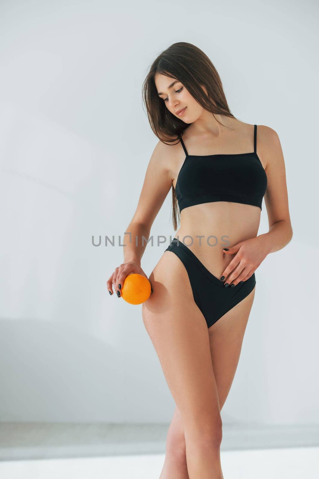 Holding orange. Beautiful woman in underwear is posing indoors.