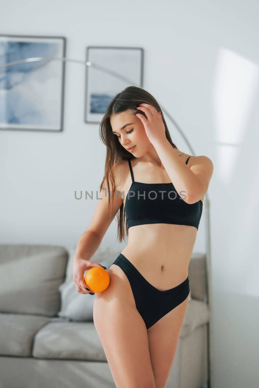 With orange in hand. Beautiful woman in underwear is posing indoors by Standret