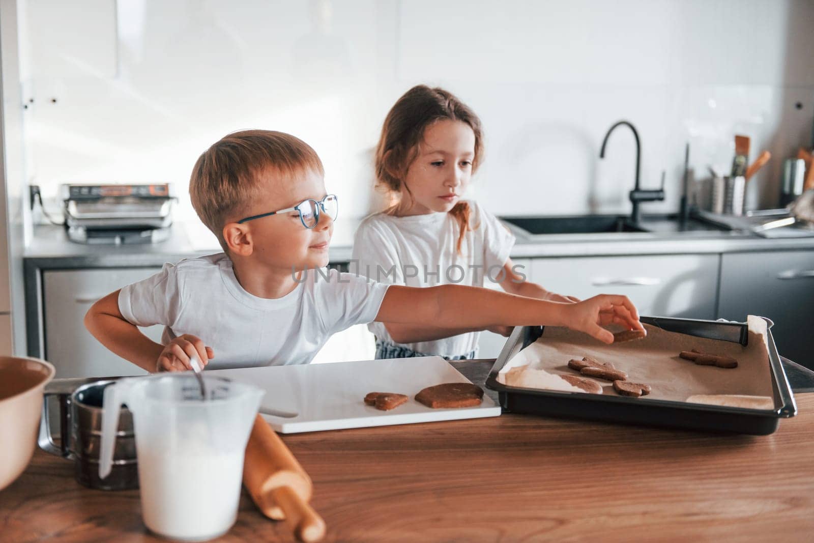 Holding cookie. Little boy and girl preparing Christmas sweets on the kitchen by Standret