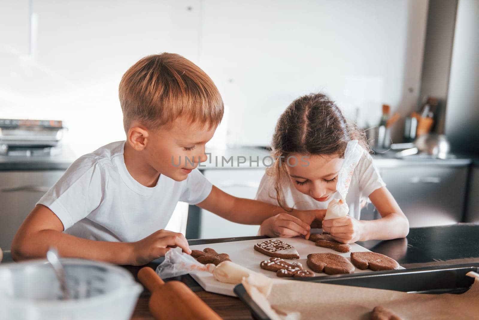 Brother and sister helping each other. Little boy and girl preparing Christmas cookies on the kitchen.