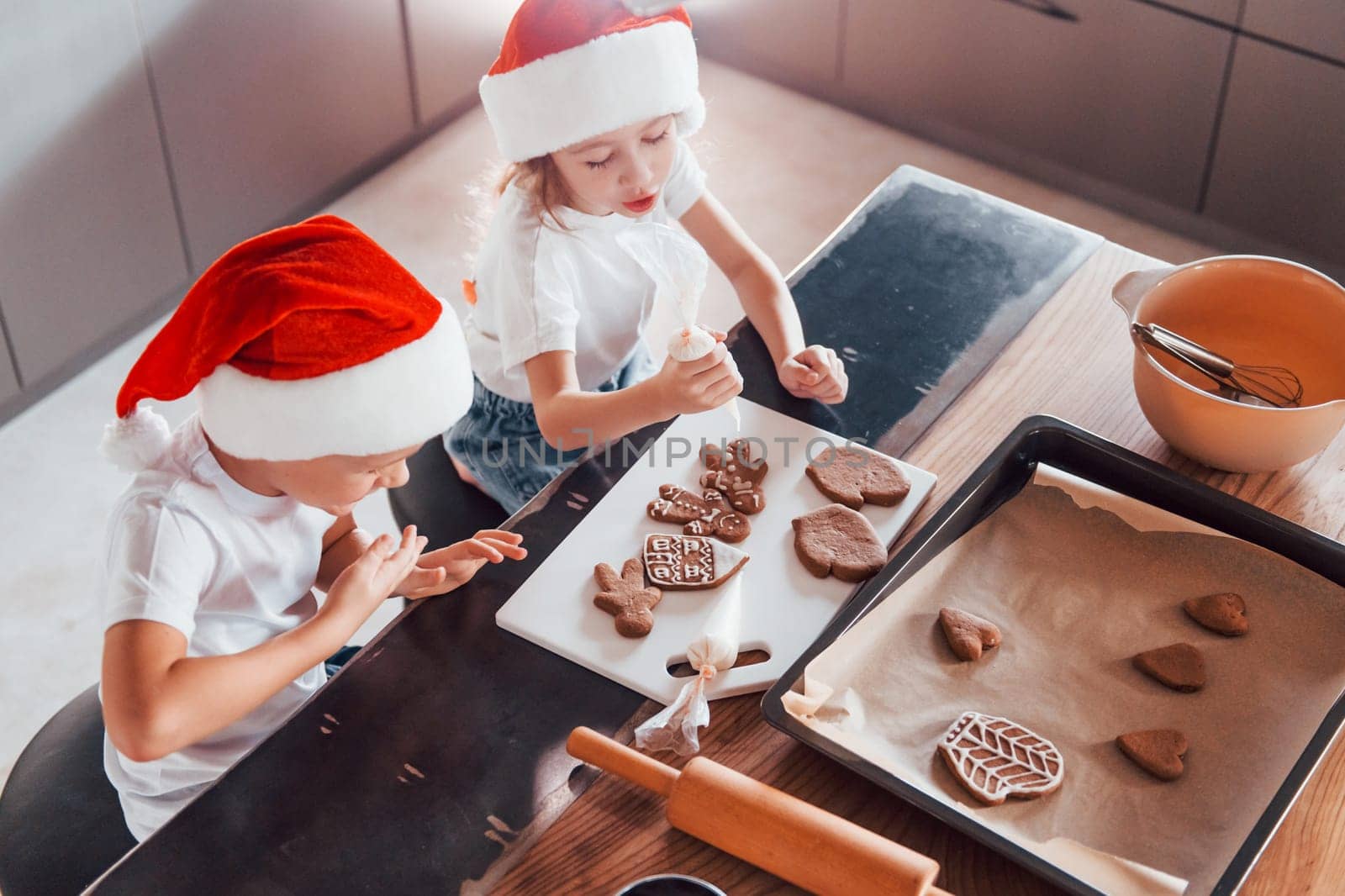 In santa hats. Little boy and girl preparing Christmas cookies on the kitchen.