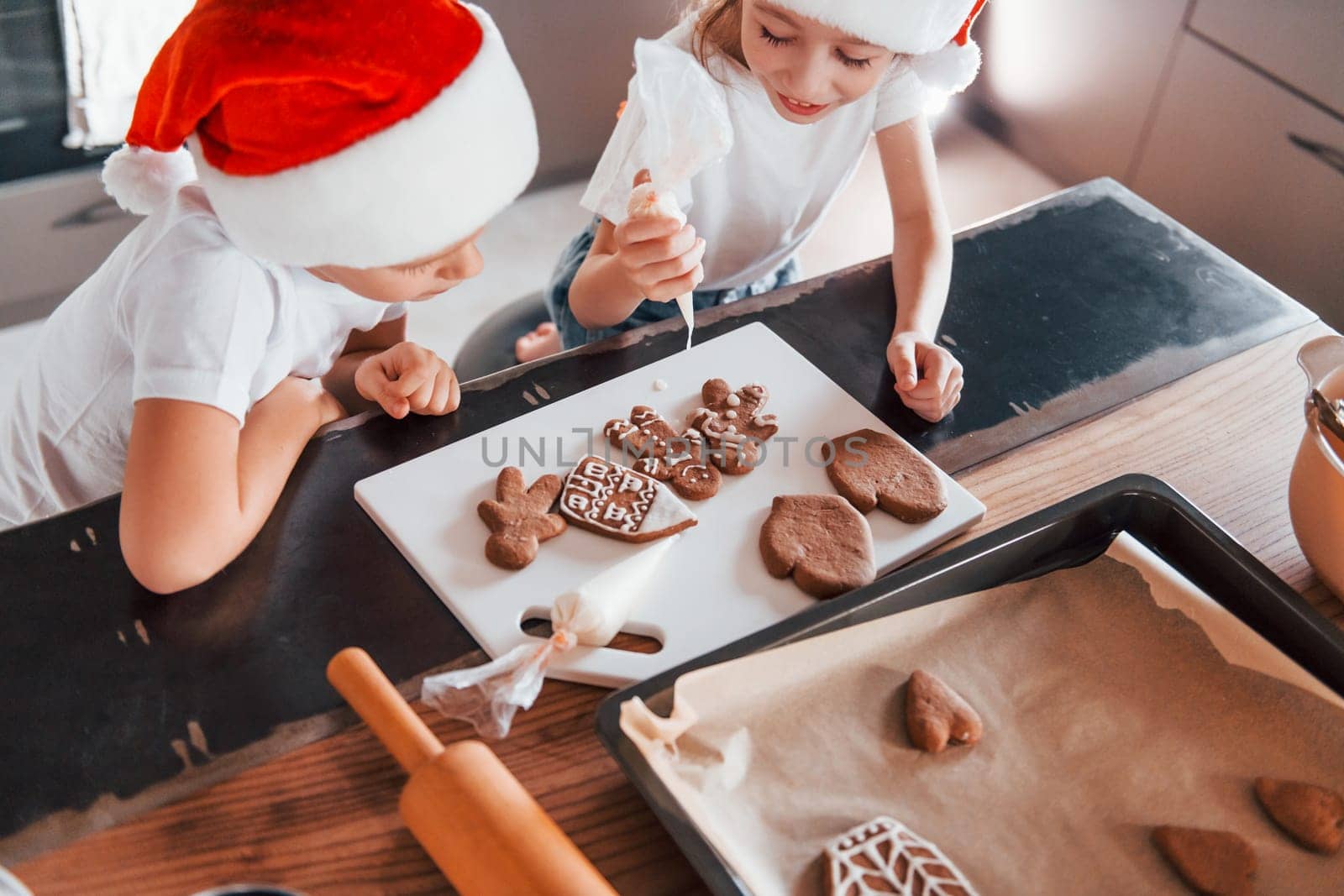 In santa hats. Little boy and girl preparing Christmas cookies on the kitchen.