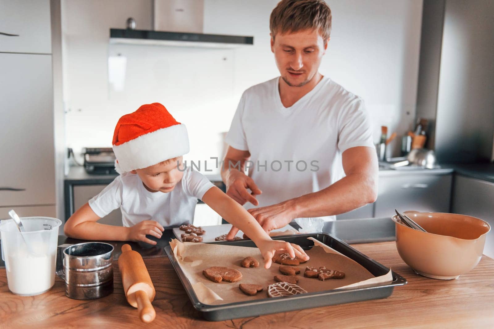 Standing by the table. Father teaching his little son with preparing of sweet christmas cookies by Standret