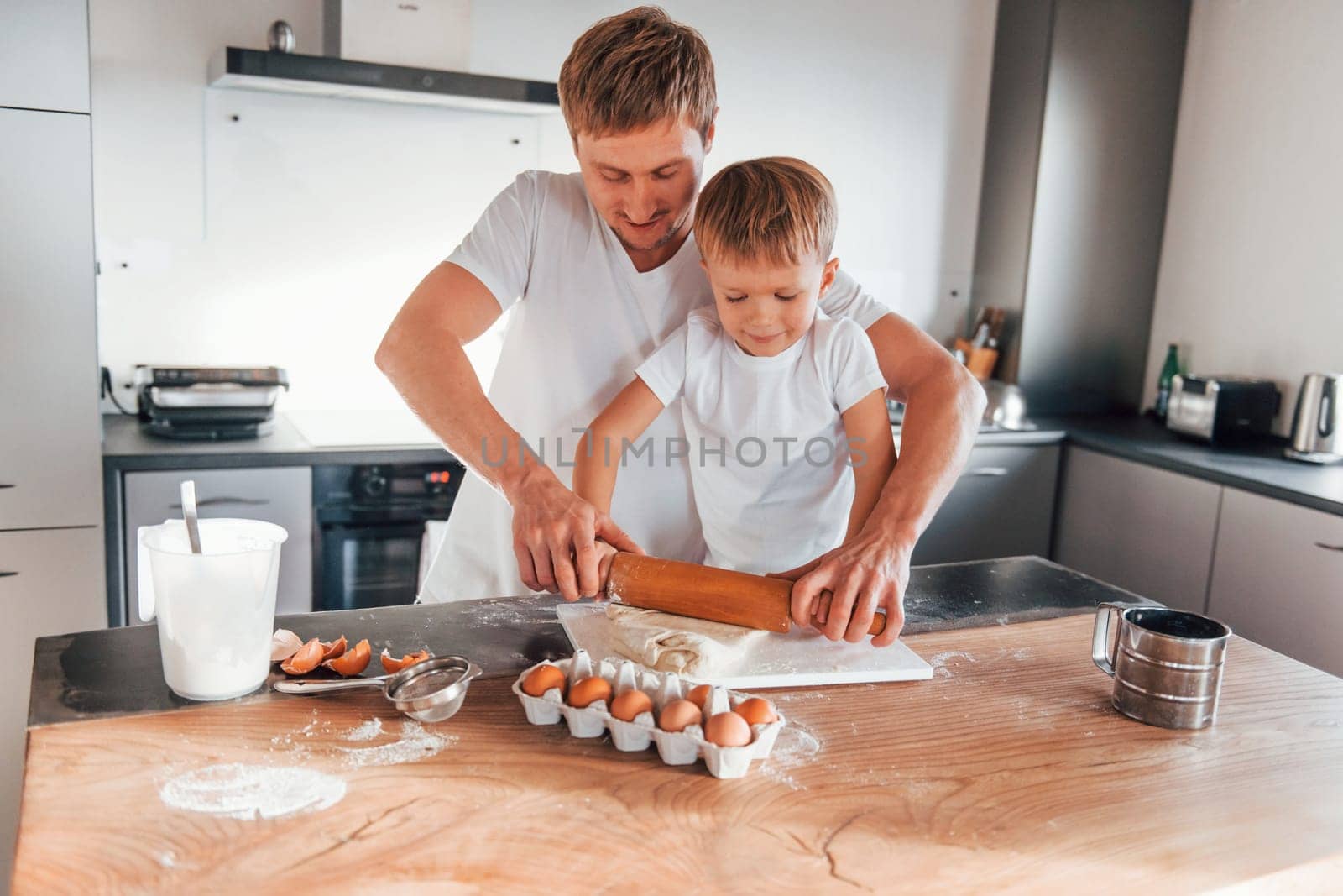 Standing by the table. Father teaching his little son with preparing of sweet christmas cookies by Standret