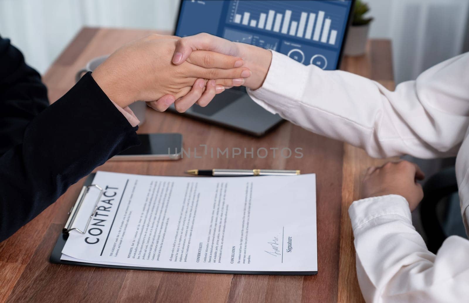 Two professionals successfully close business deal with closeup handshake, sealing the partnership agreement. Legal document and signature as formal agreement between the two companies. Enthusiastic