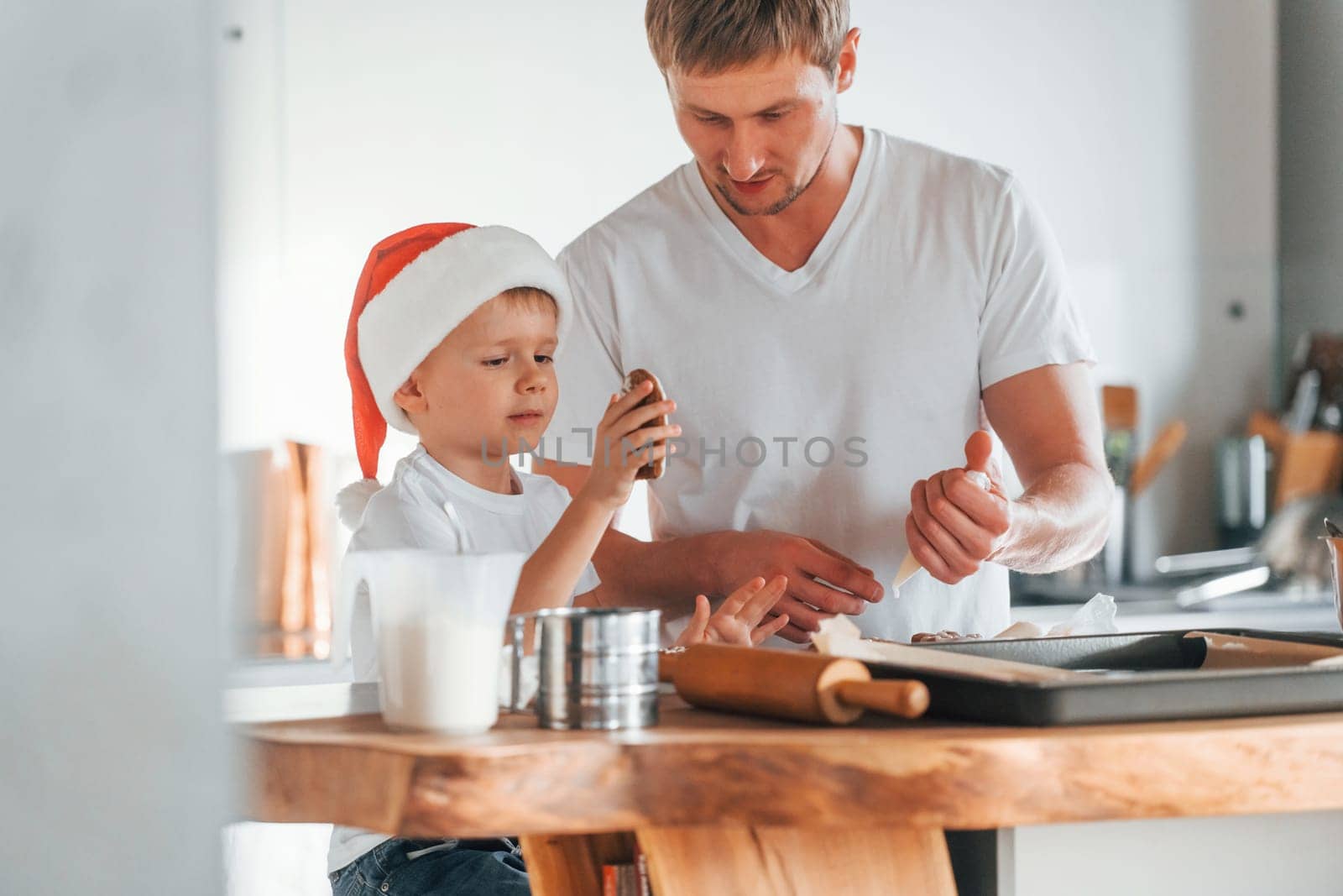 Father teaching his little son with preparing of sweet christmas cookies.