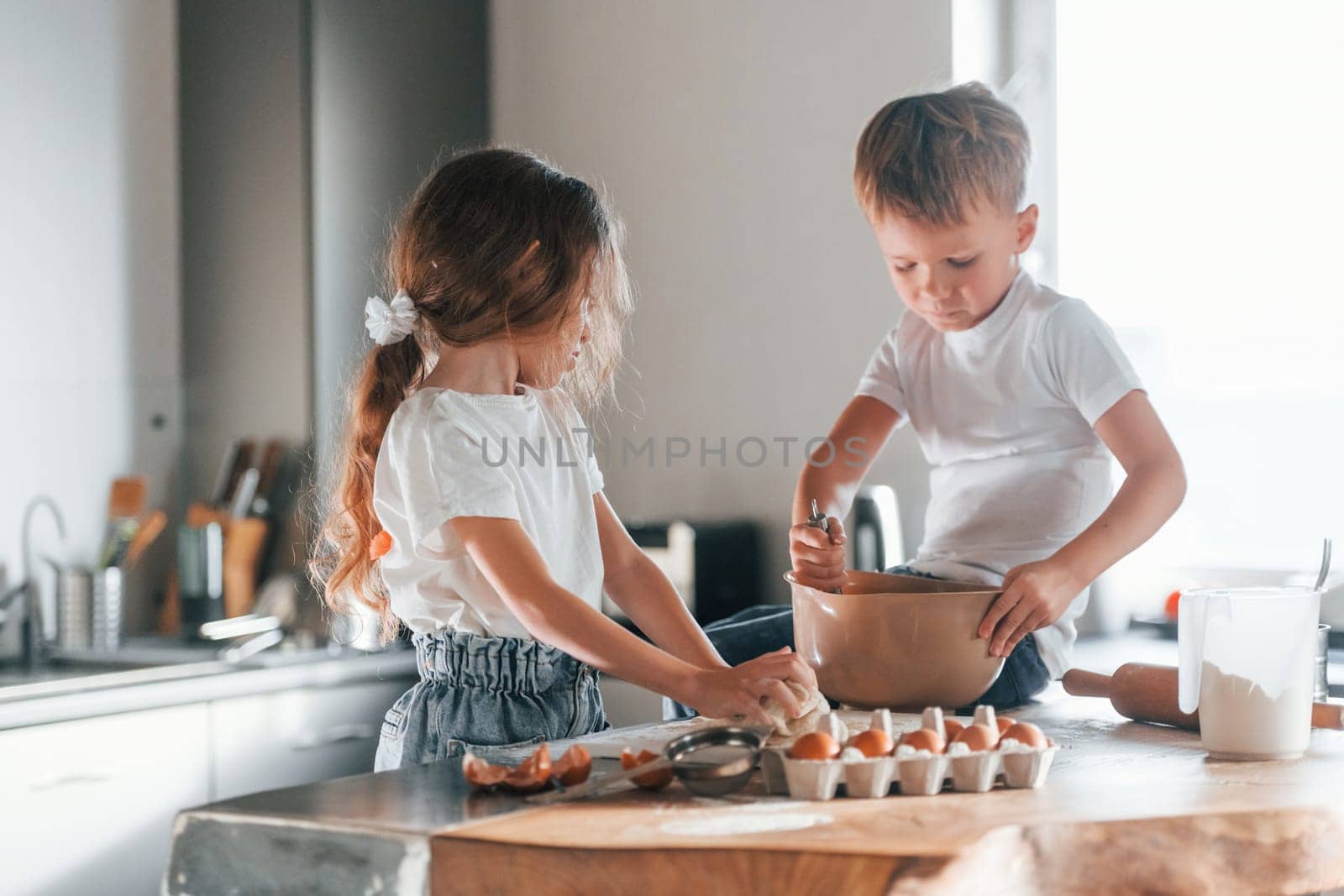 Sitting on the table. Little boy and girl preparing Christmas cookies on the kitchen by Standret