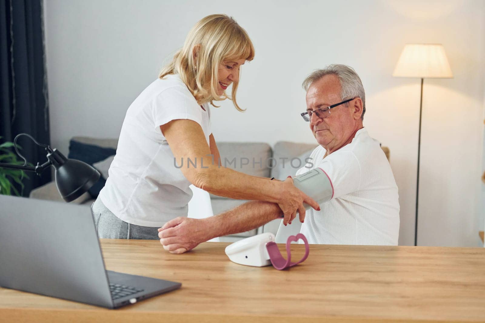Wife measuring blood preasure of her husband. Senior man and woman is together at home.