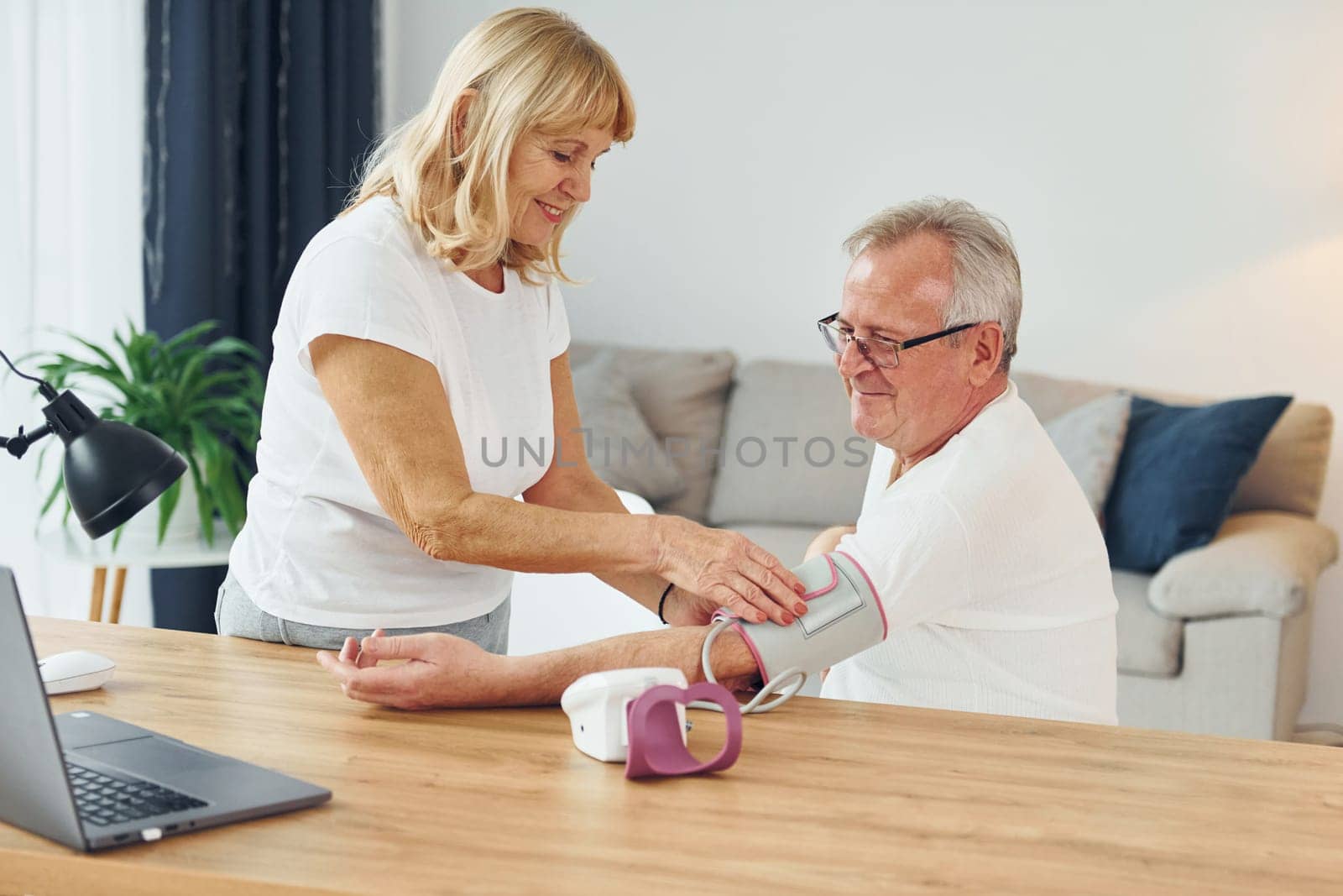 Wife measuring blood preasure of her husband. Senior man and woman is together at home by Standret
