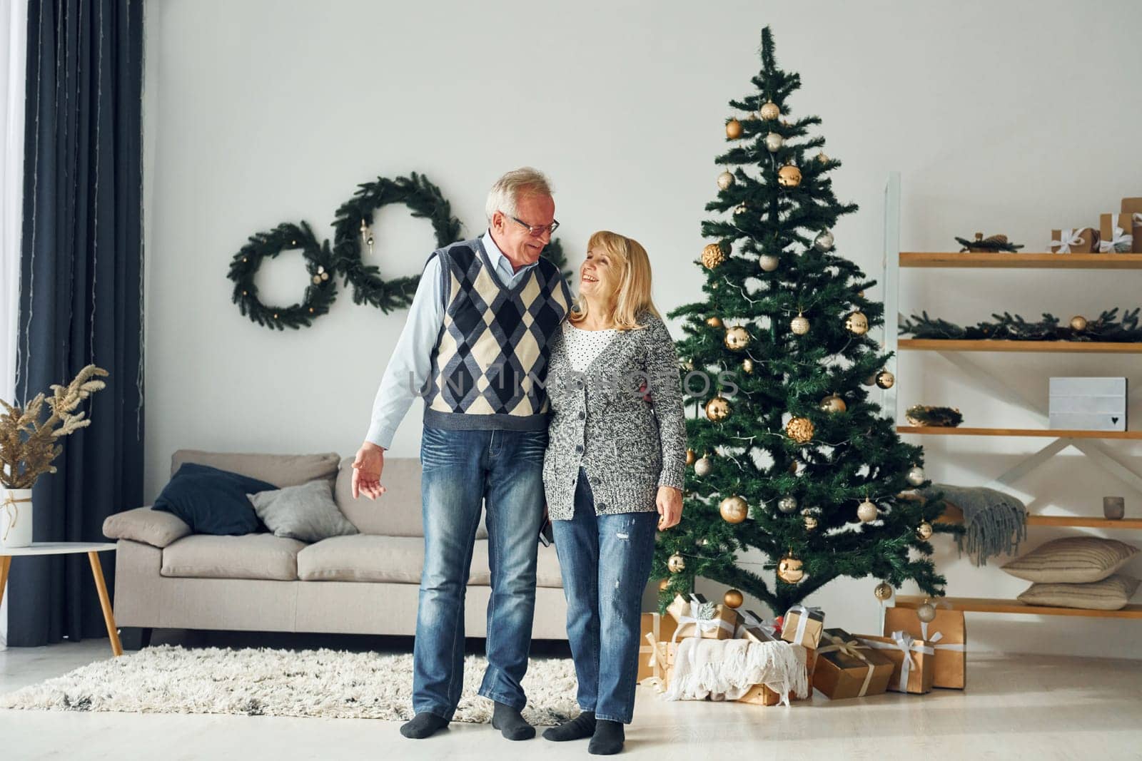 Standing near christmas tree. Senior man and woman is together at home.