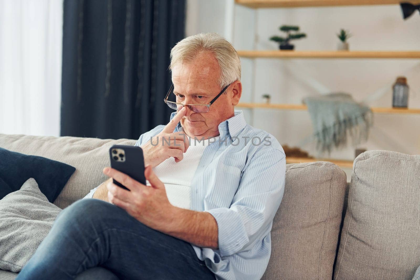 Sitting with smartphone in hands. Senior man in nice clothes is at home.