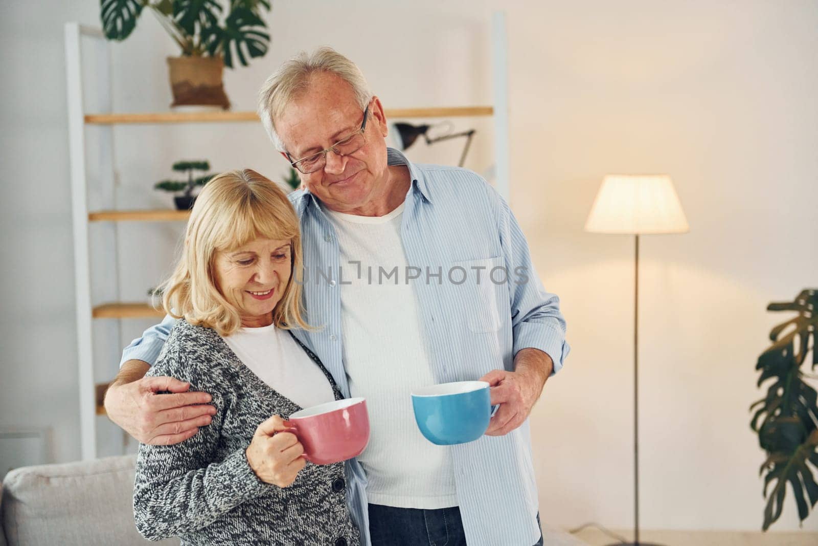 Standing and holding cups of drinks. Senior man and woman is together at home.