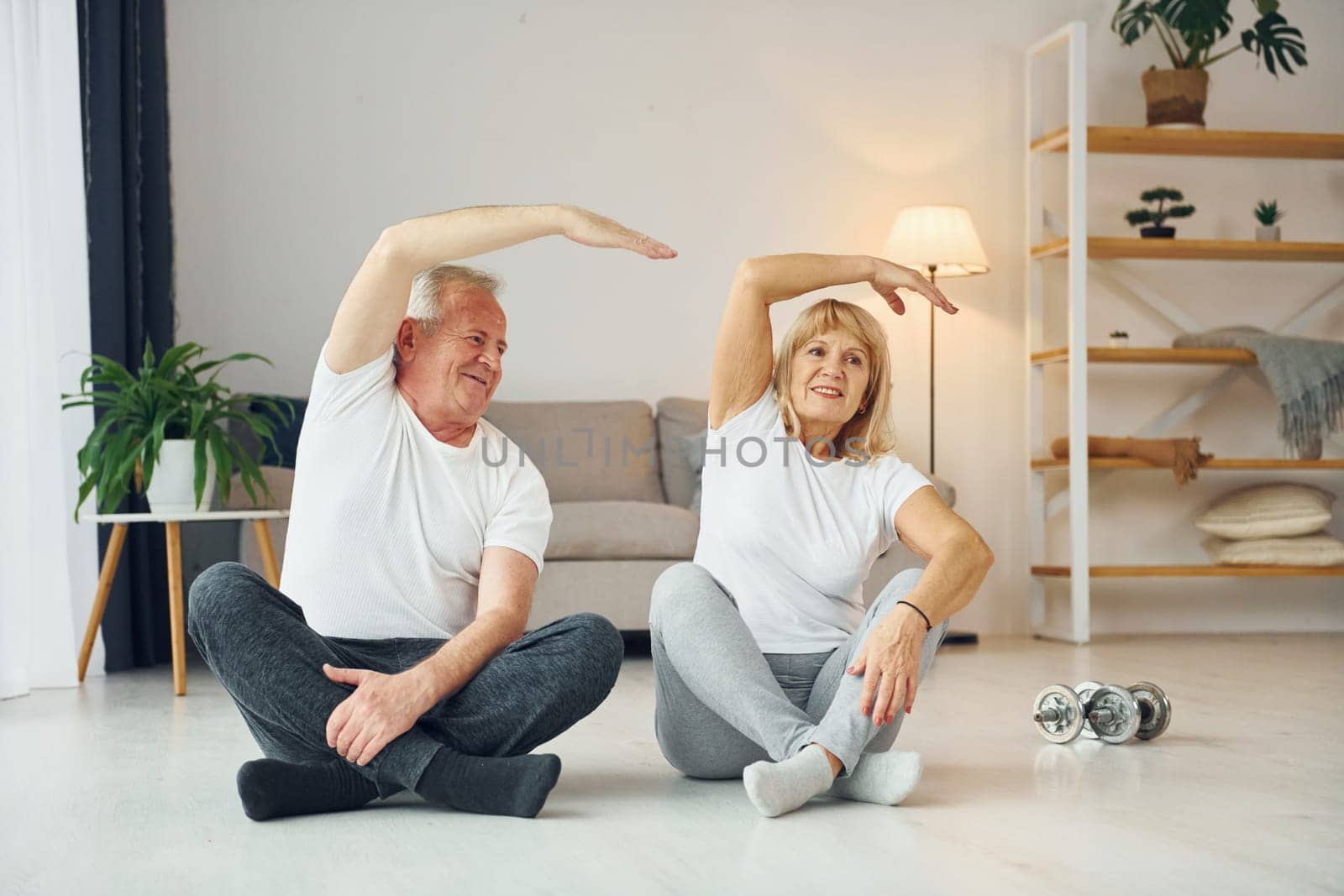 Sitting and doing exercises. Senior man and woman is together at home.