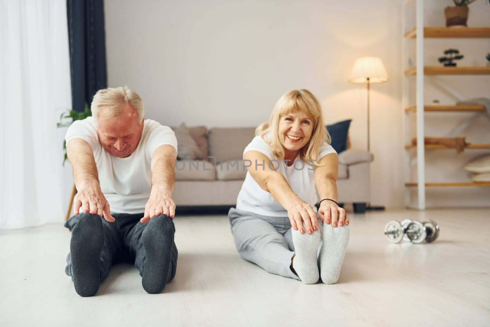 Sitting and doing exercises. Senior man and woman is together at home by Standret