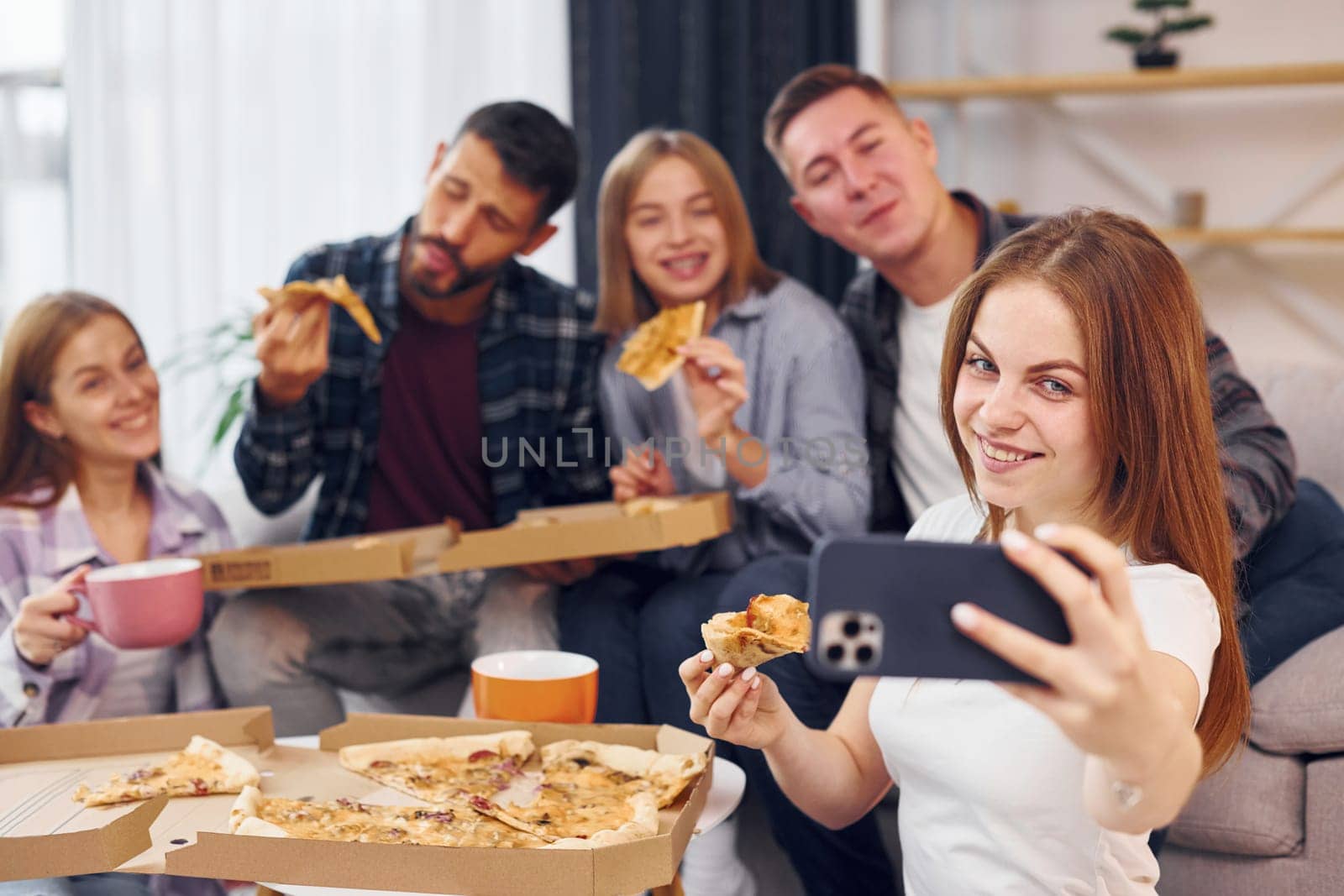 Woman making selfie. Group of friends have party indoors together.