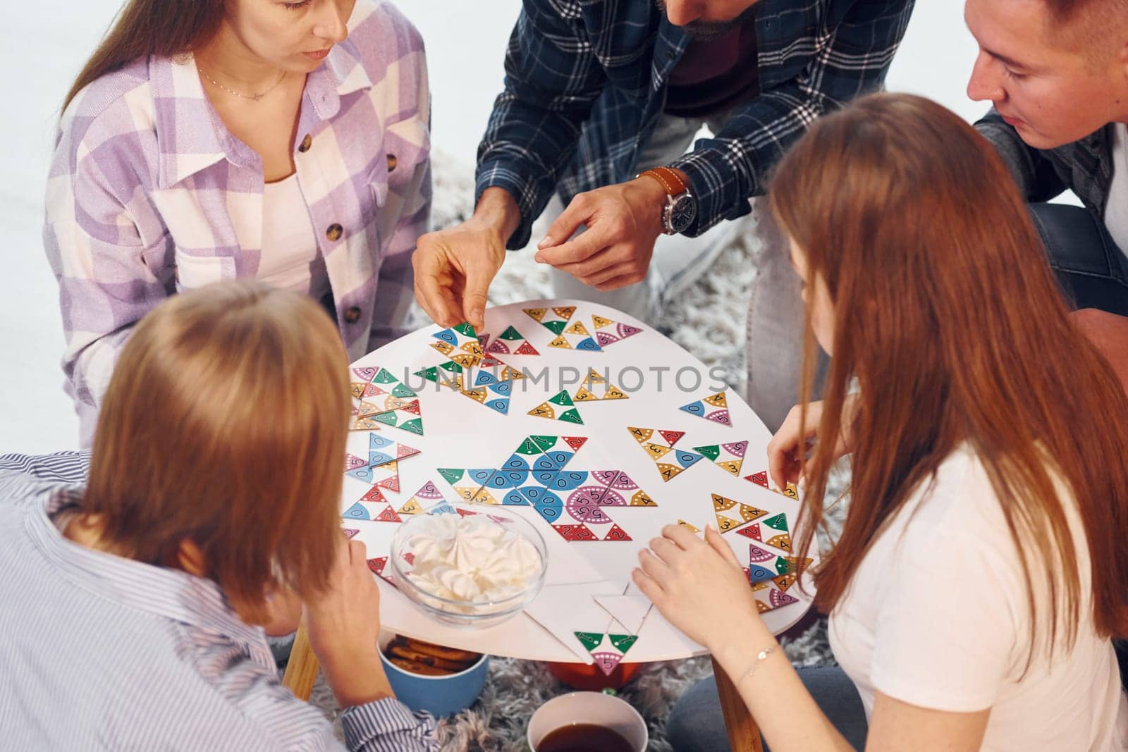 Playing puzzle game. Group of friends have party indoors together.